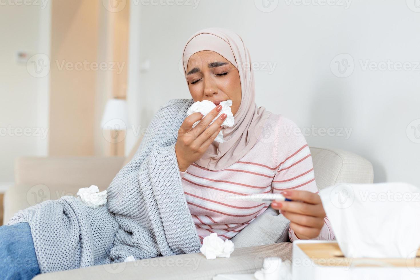 Arabisch vrouw is hebben griep en ze is gebruik makend van thermometer. ziek met een rhinitis vrouw met hijab heeft druipend neus. vrouw wezen ziek hebben griep aan het liegen Aan sofa op zoek Bij temperatuur Aan thermometer. foto