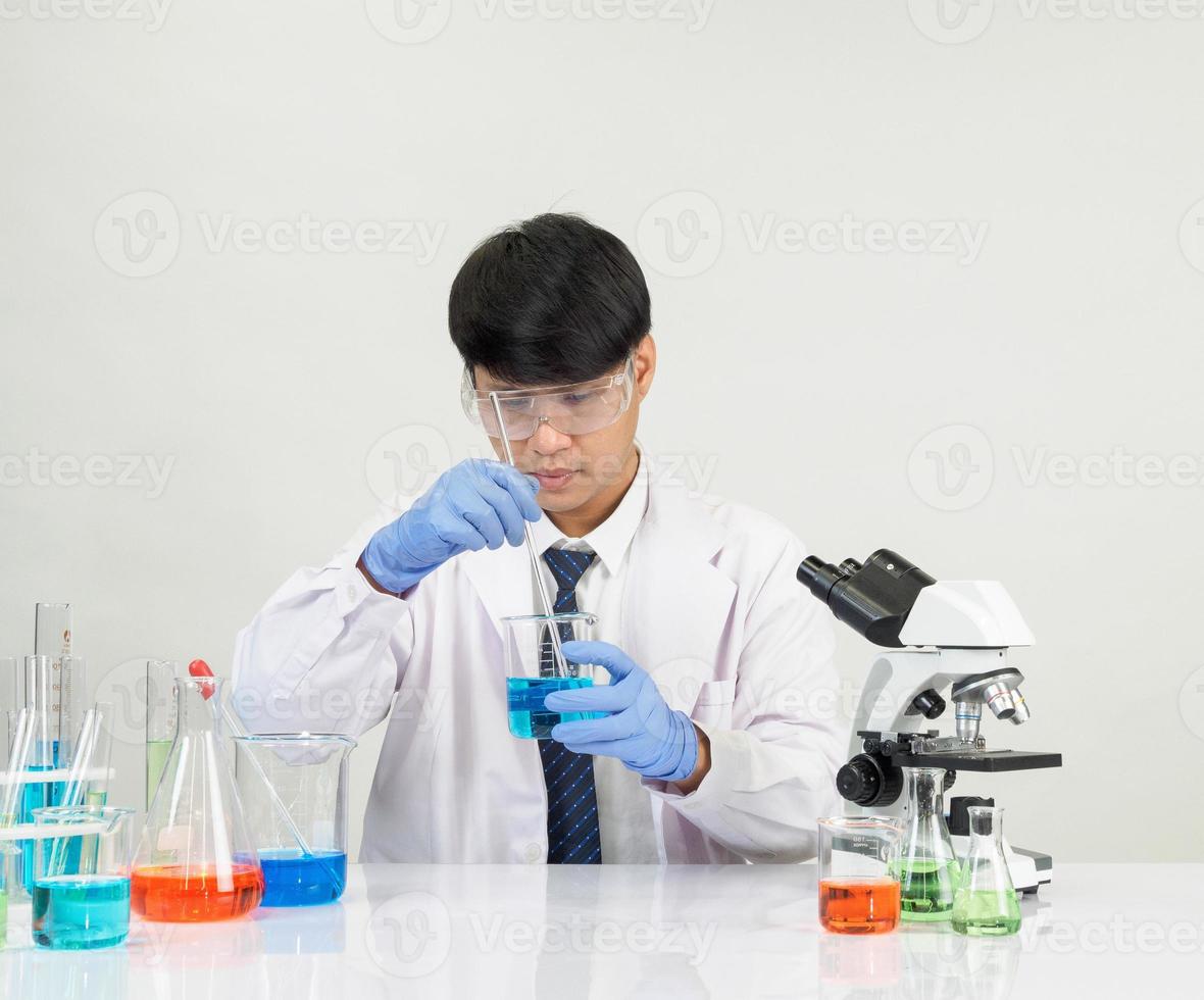 Aziatisch mannetje leerling wetenschapper in reagens menging laboratorium in een wetenschap Onderzoek laboratorium met test buizen van divers maten en microscopen. Aan de tafel in laboratorium chemie laboratorium wit achtergrond. foto