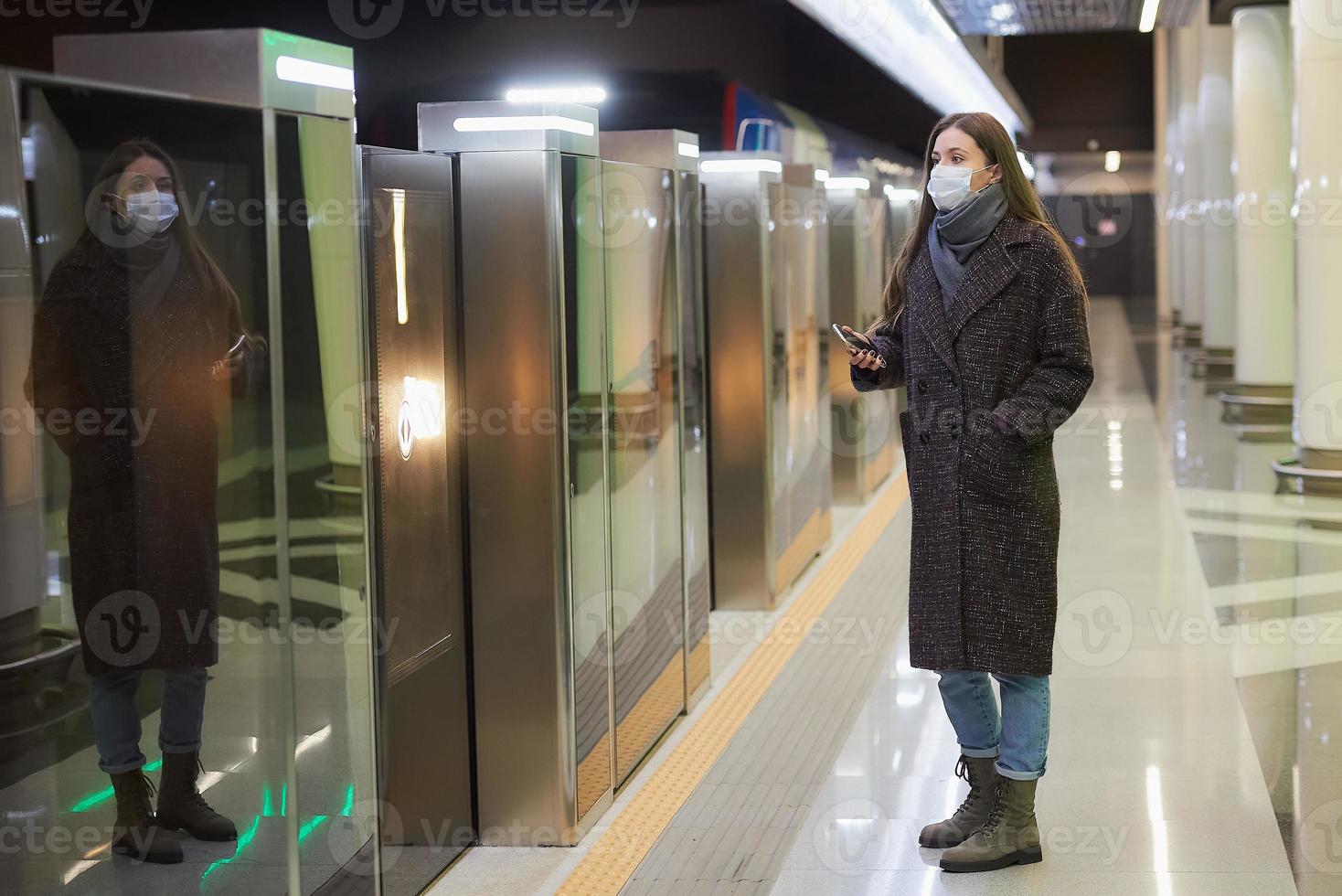 een vrouw met een medisch gezichtsmasker wacht in de metro op een aankomende trein foto