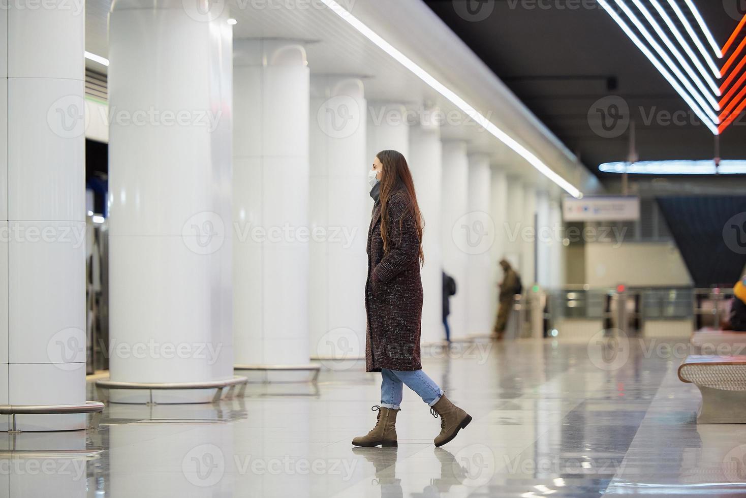 een meisje met een chirurgisch gezichtsmasker houdt sociale afstand in een metrostation foto