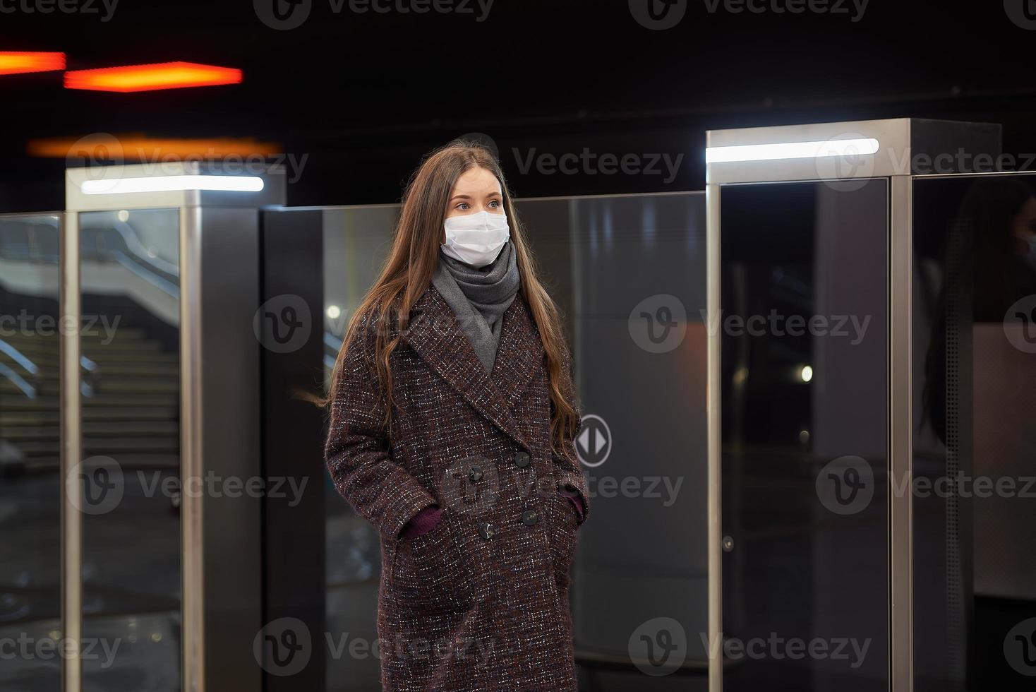 vrouw in een medisch gezichtsmasker staat in de buurt van de vertrekkende trein in de metro foto