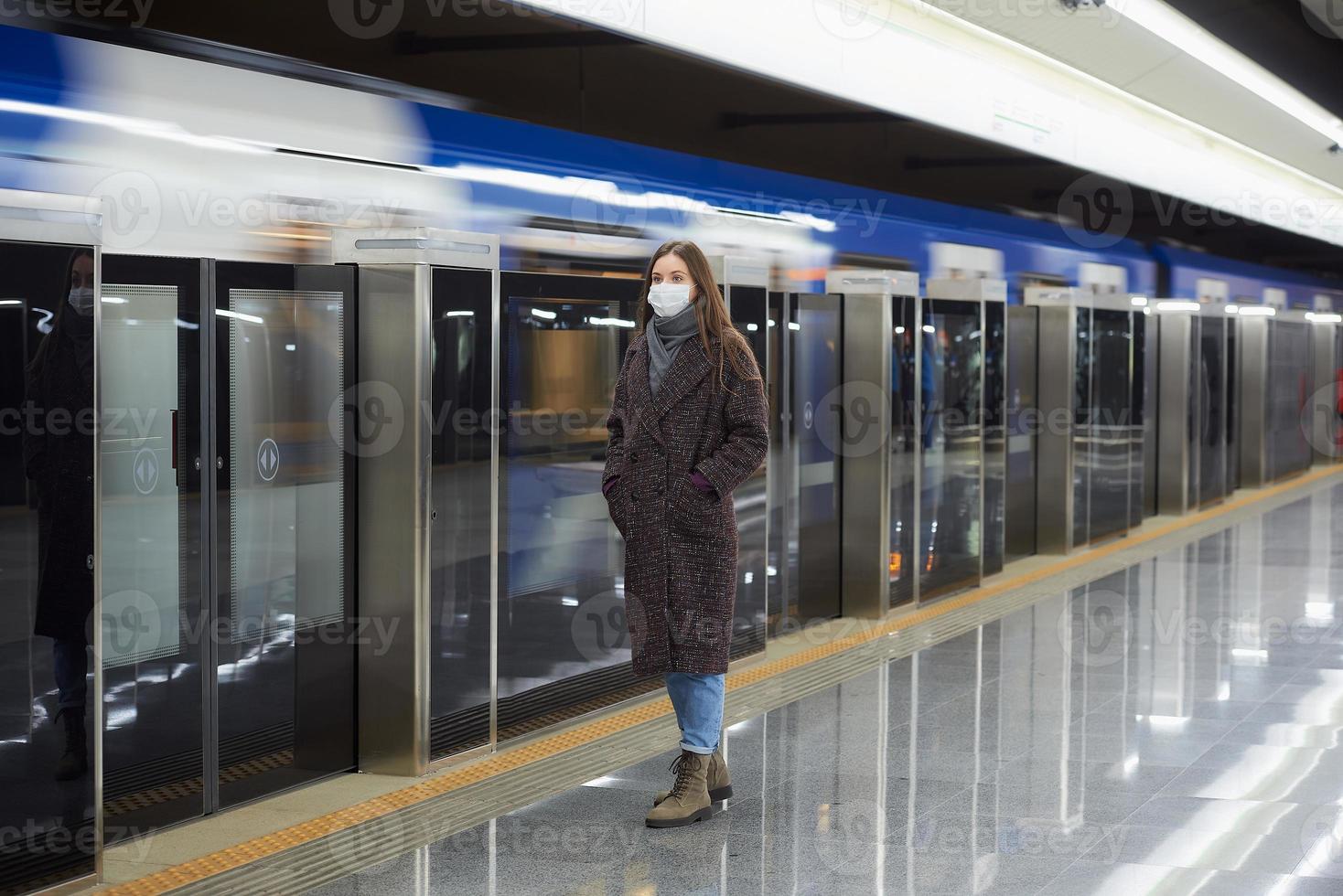 een vrouw met een medisch gezichtsmasker wacht in de metro op een aankomende trein foto