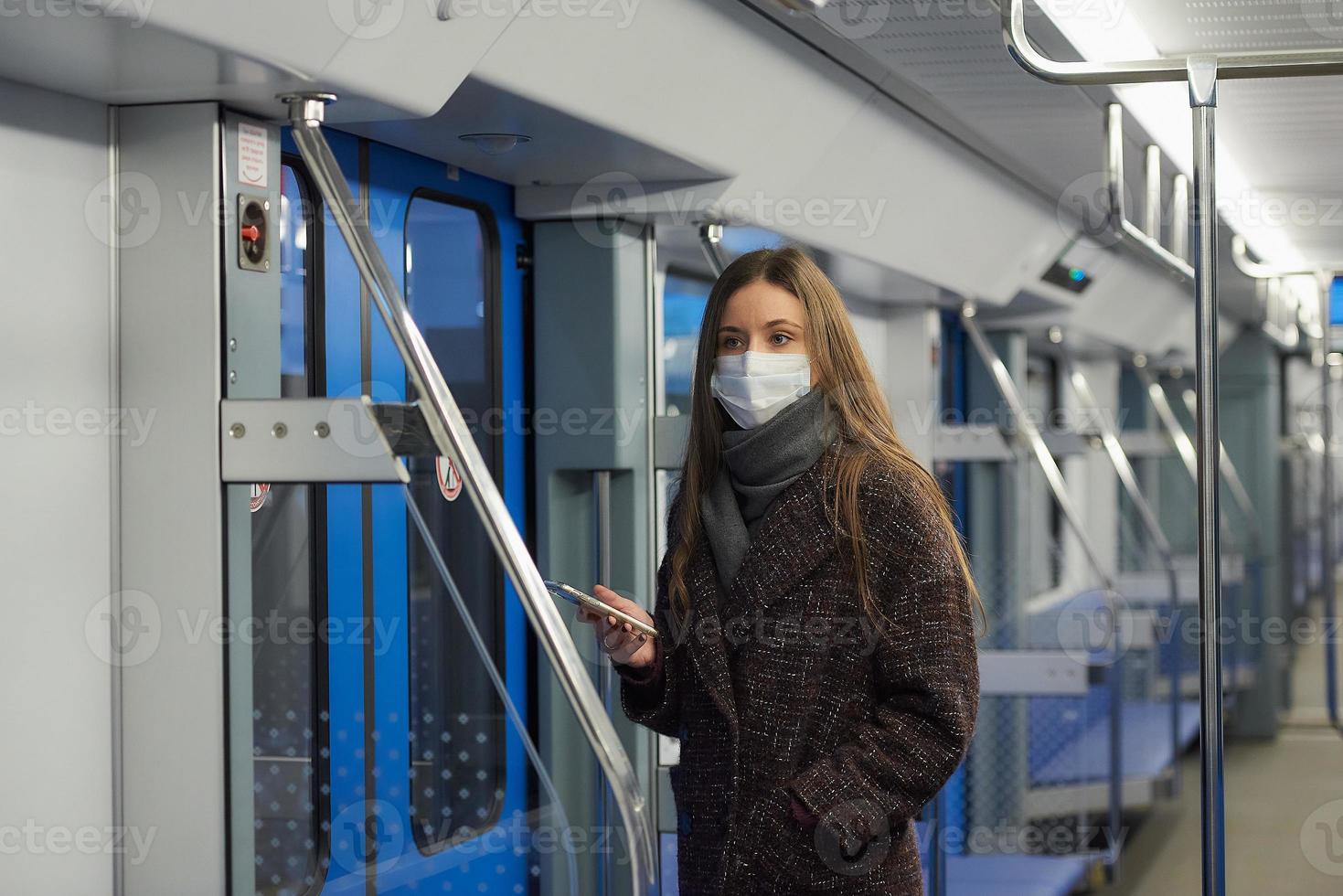 een vrouw met een gezichtsmasker staat en gebruikt een smartphone in een moderne metro foto