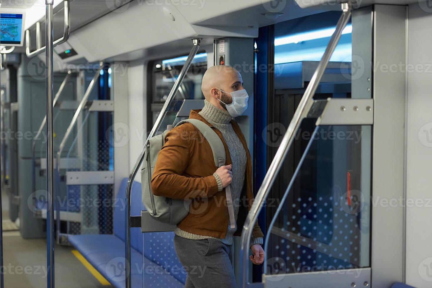 een kale man met een baard in een gezichtsmasker verlaat een metro foto