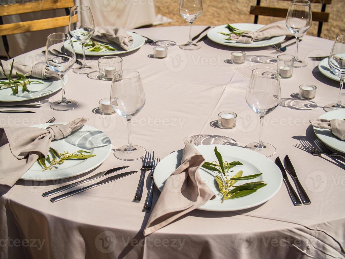bruiloft banket concept. stoelen en ronde tafel voor gasten, geserveerd met messenmaker en, bloemen en serviesgoed en gedekt met een tafelkleed foto