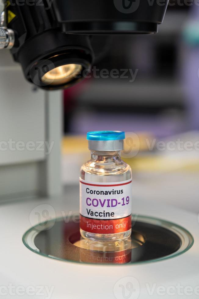 Covid-19-vaccinfles met microscoop in laboratorium foto