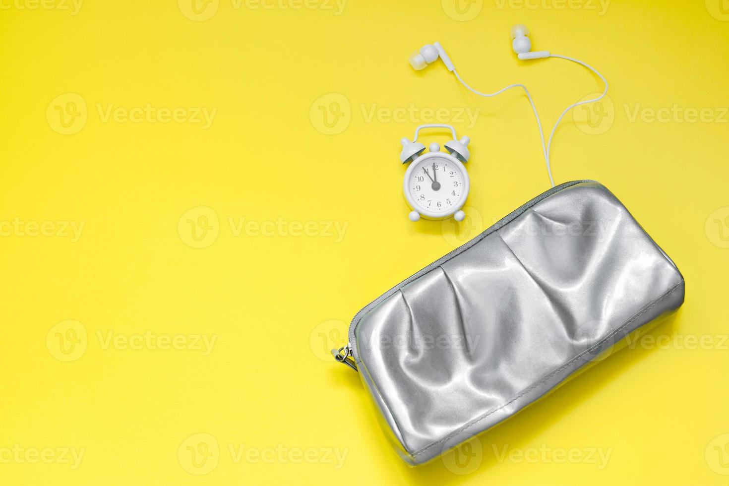 zilveren cosmetische tas, wekker en koptelefoon op gele achtergrond foto
