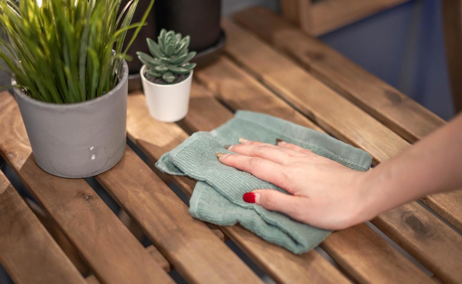 dichtbij omhoog vrouw hand- schoonmaak houten tafel gebruik makend van ontsmettingsmiddel groen handdoek. voorkomen infectie van covid-19 virus, besmetting van kiemen of bacteriën, veeg of schoonmaak naar elimineren. foto