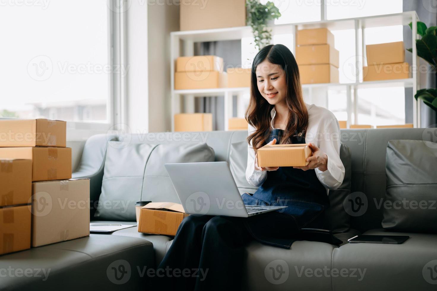 jong Aziatisch bedrijf eigenaar vrouw bereiden pakket doos en staand controleren online bestellingen voor leveren naar klant Aan tablet, laptop boodschappen doen online concept. foto