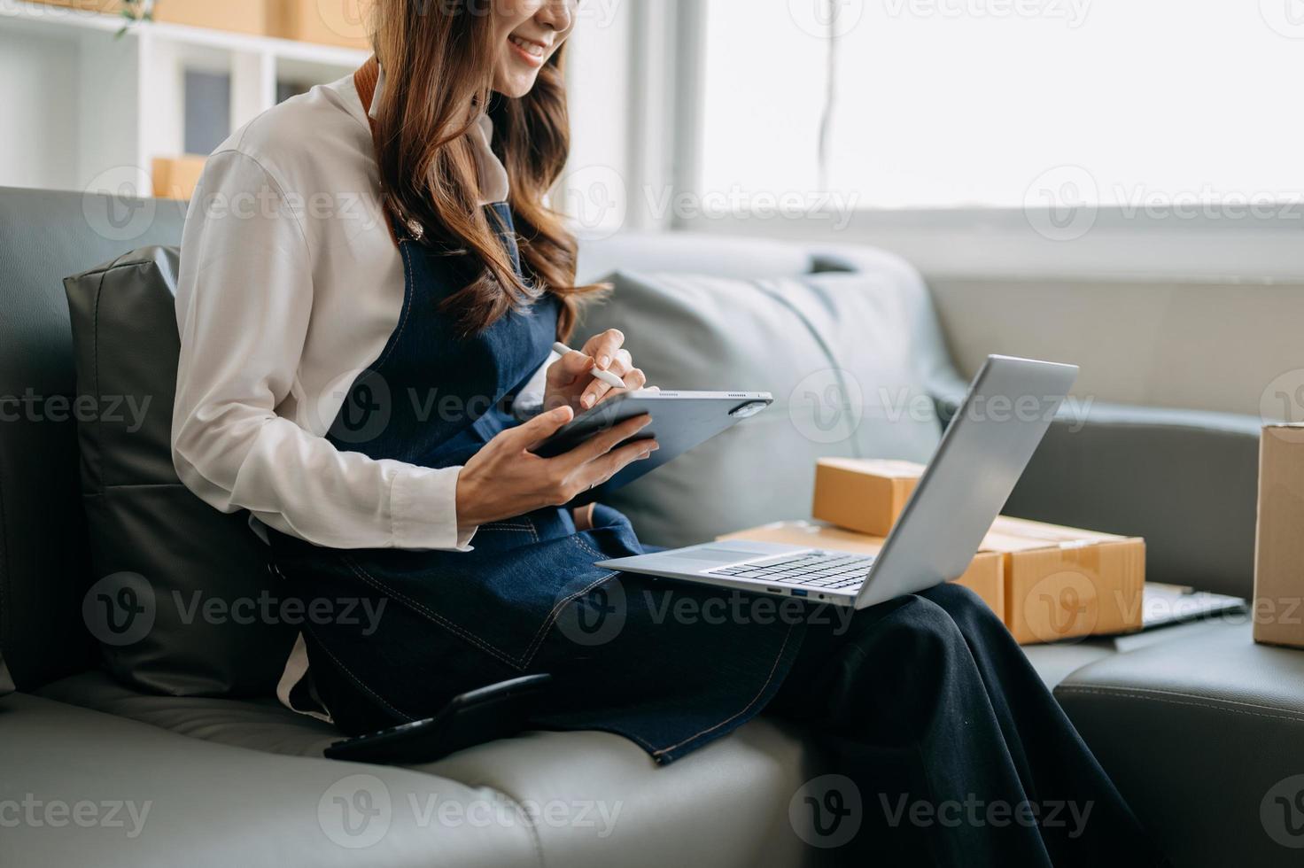 vrouw hand- gebruik makend van een laptop, smartphone en tablet en schrijven notitieboekje Bij de kantoor van haar bedrijf online winkelen. in huis foto