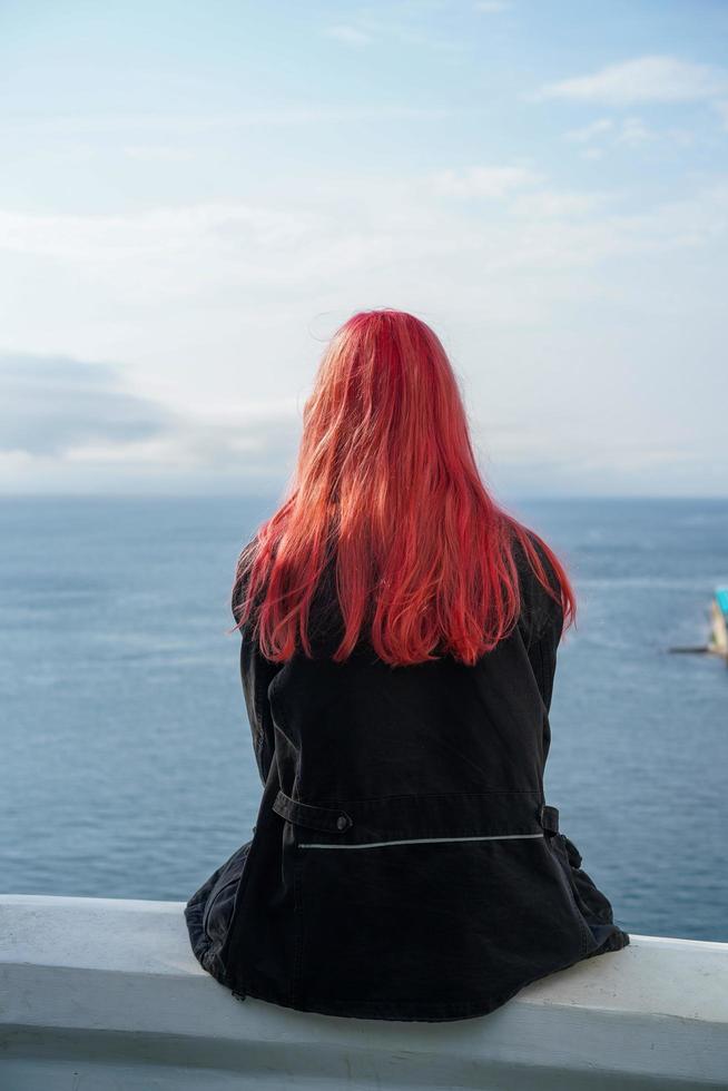 een meisje met roze haar zit met haar rug tegen de zee. foto