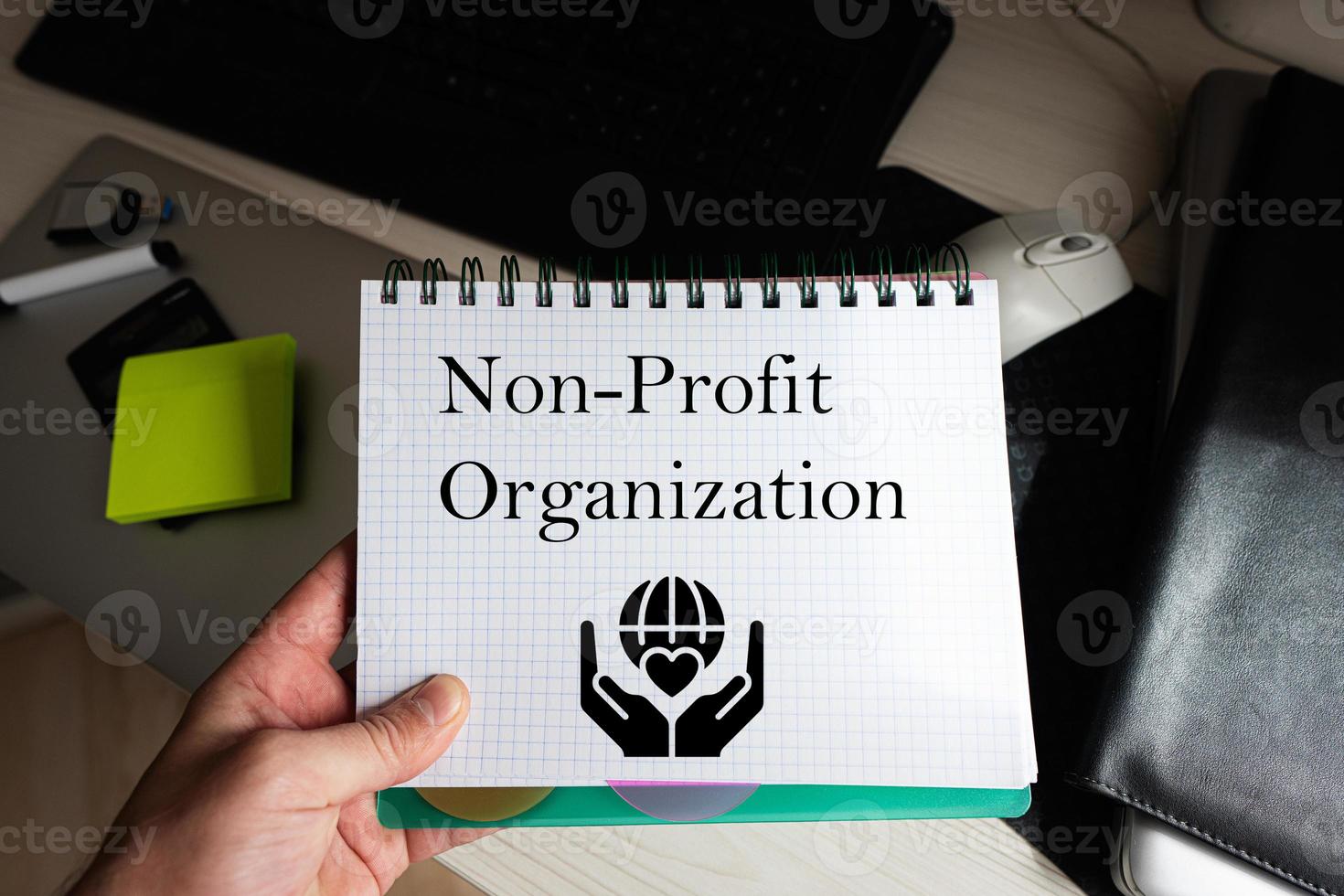 non-profit organisatie woord Aan notitieboekje Holding Mens tegen bureaublad. foto
