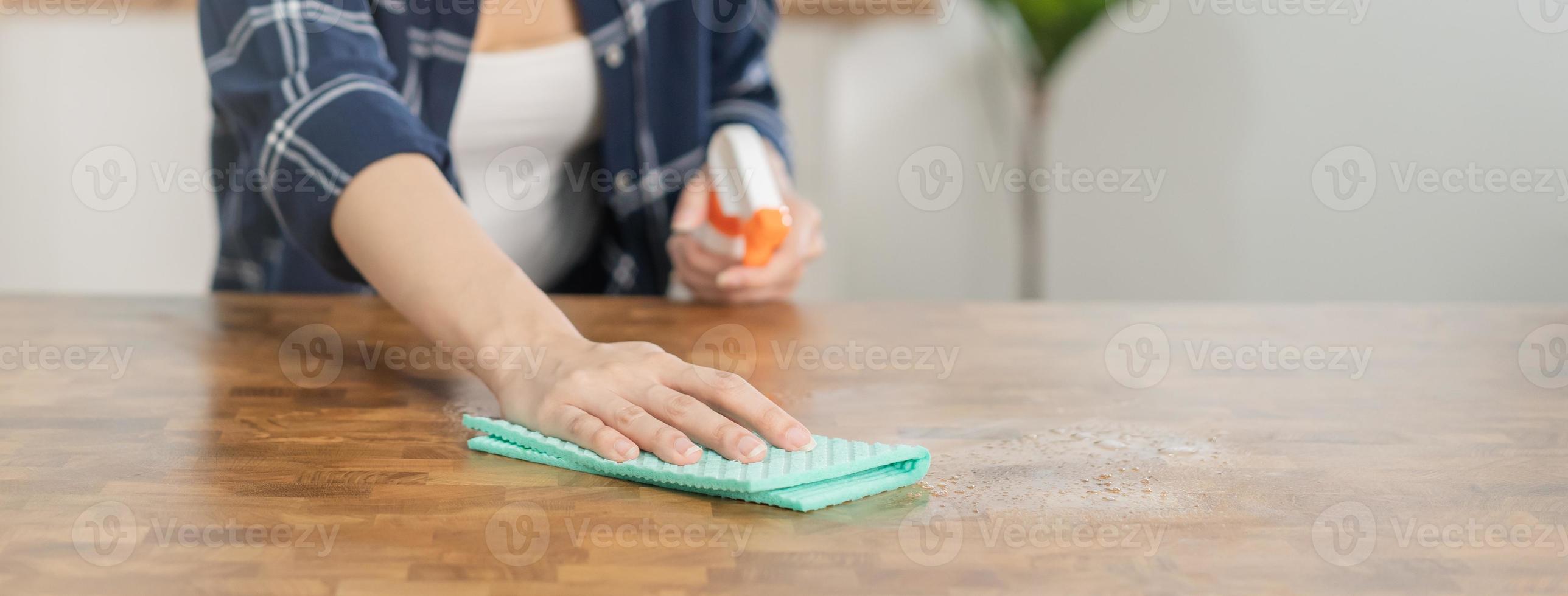 hand- van Aziatisch jong vrouw hand- schoonmaak houten tafel, kastje, gebruik makend van vod wrijven stof, Holding verstuiven fles in keuken Bij huis. huishouden hygiëne schoon omhoog, schoonmaakster mensen, uitrusting of gereedschap voor schoonmaak. foto