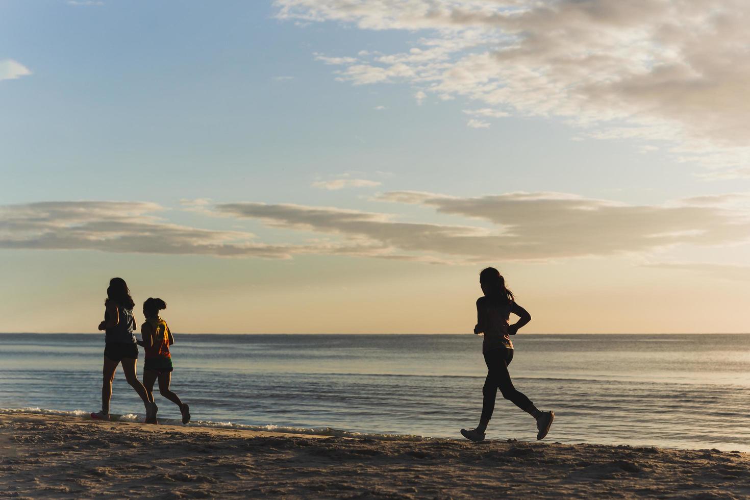 silhouet van drie vrouw jogging Aan de strand Bij zonsopkomst. foto
