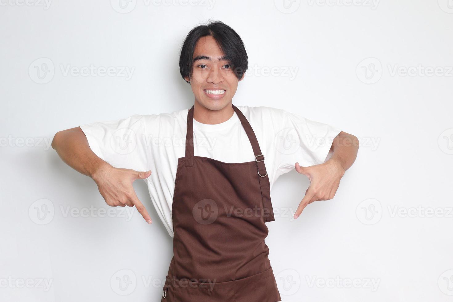 portret van aantrekkelijk Aziatisch barista Mens in bruin schort tonen Product, richten Bij iets met handen. reclame concept. geïsoleerd beeld Aan wit achtergrond foto
