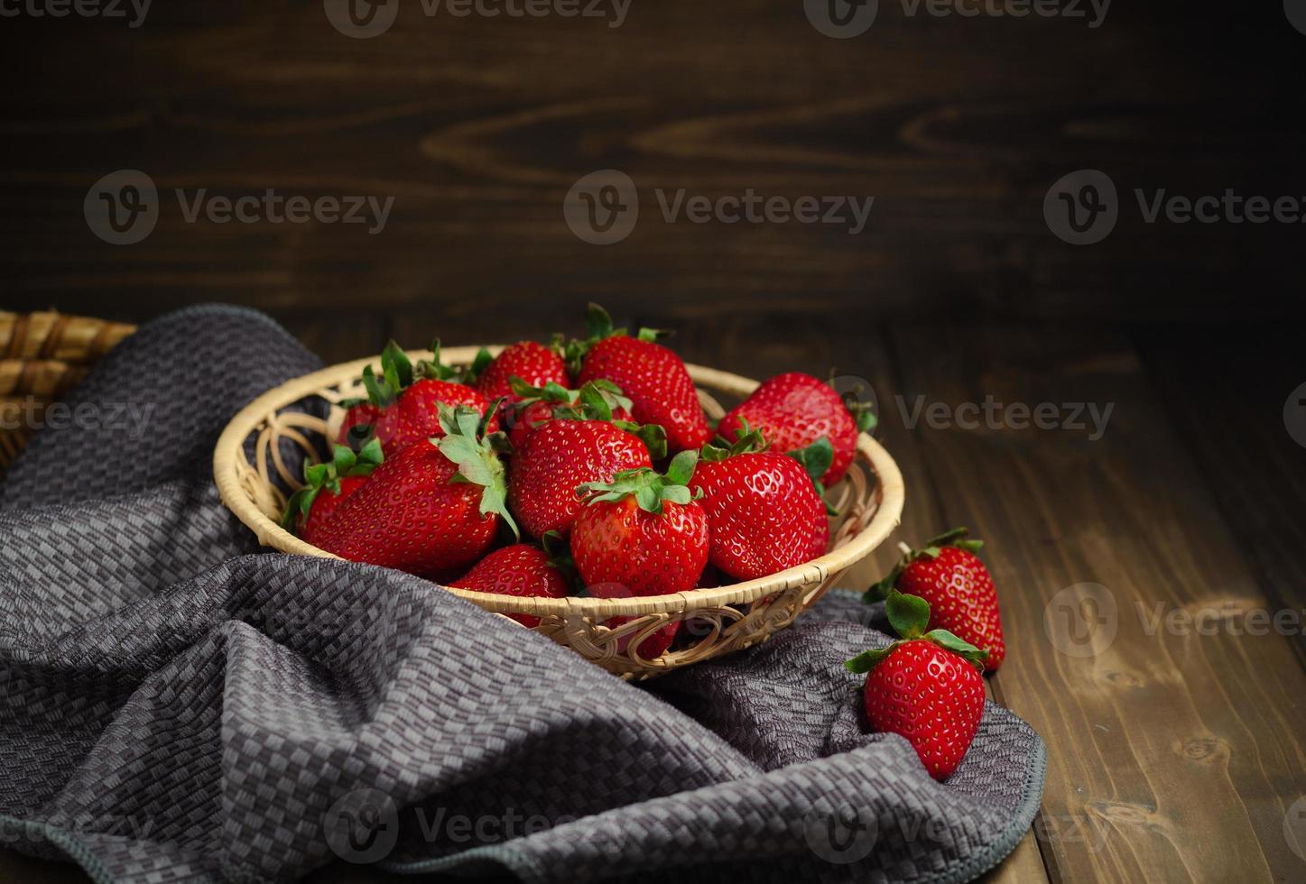 rieten mand met zoet rood aardbeien Aan een donker houten tafel. foto