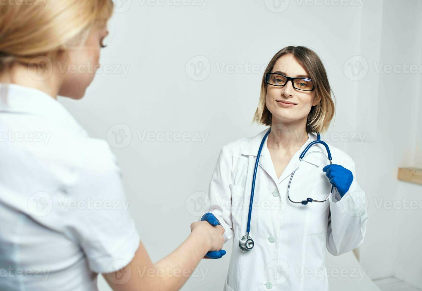 de verpleegster schudt handen met de geduldig Aan een licht achtergrond en blauw handschoenen met een stethoscoop foto