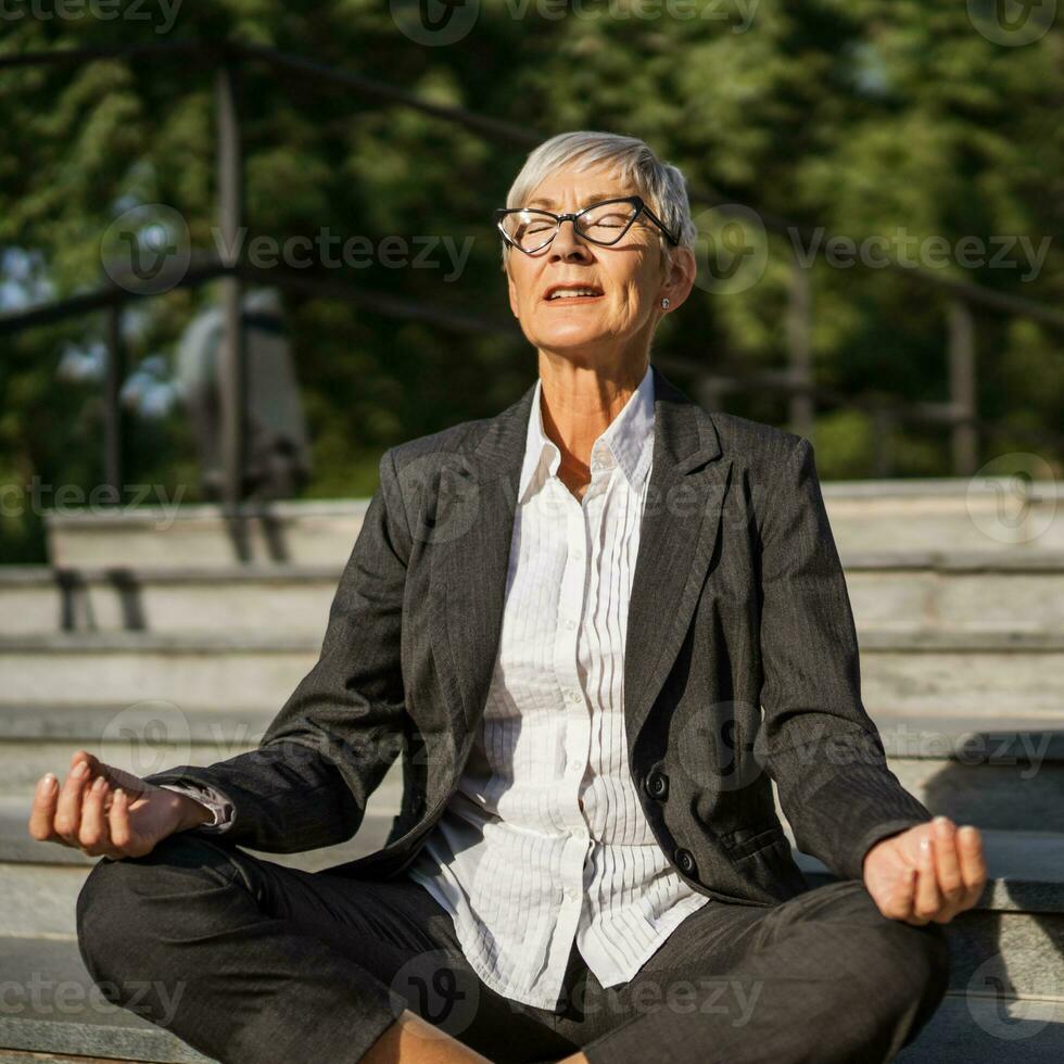 buitenshuis portret van senior zakenvrouw wie is mediteren in voorkant van bedrijf gebouw. foto