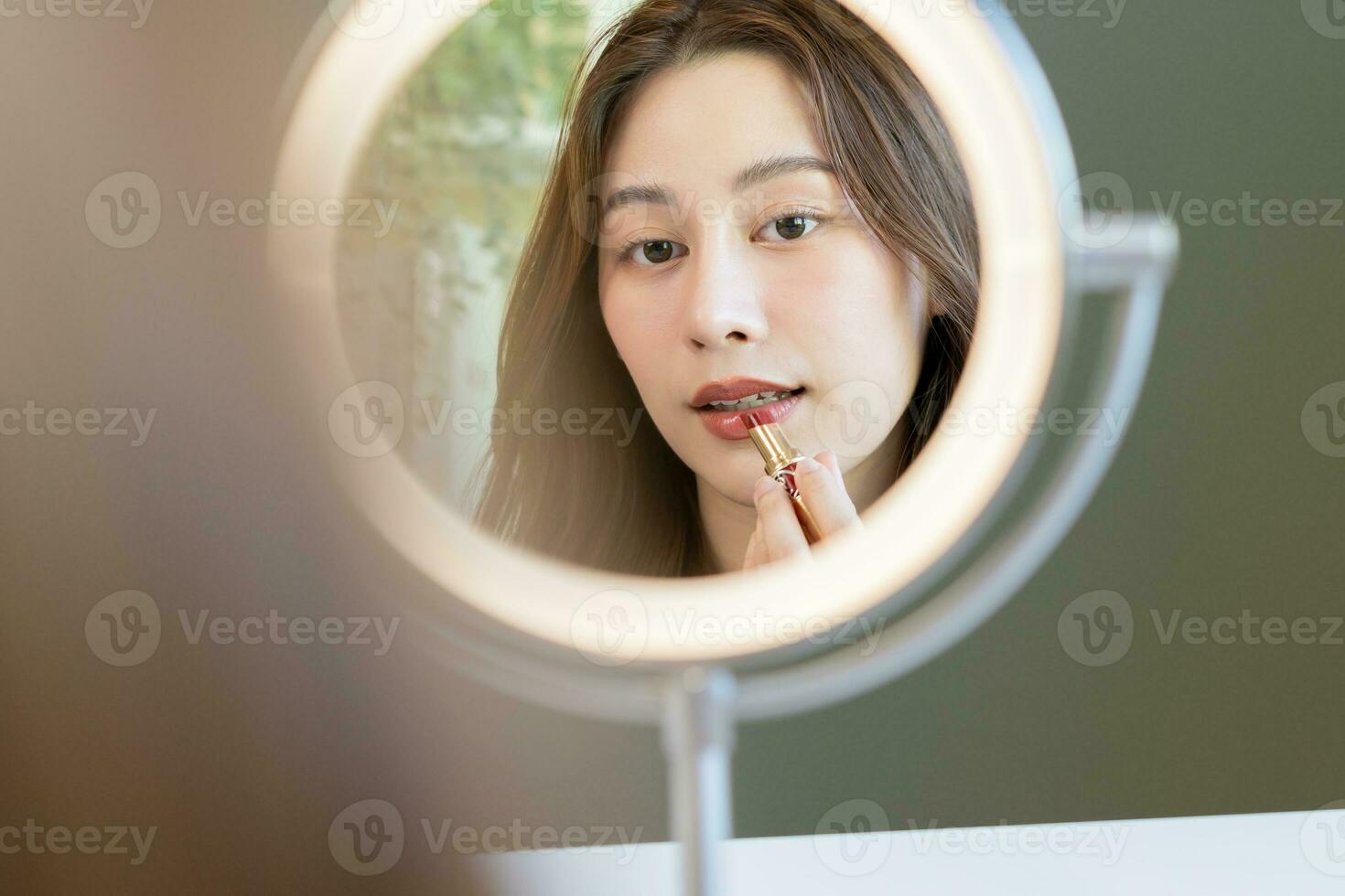 huid zorg schoonheidsmiddelen concept, hand- van vrouw, meisje maken omhoog gezicht door toepassen rood lippenstift, lippen balsem Aan haar mond, op zoek Bij de spiegel Bij huis. vrouw kijken met natuurlijk mode stijl. foto