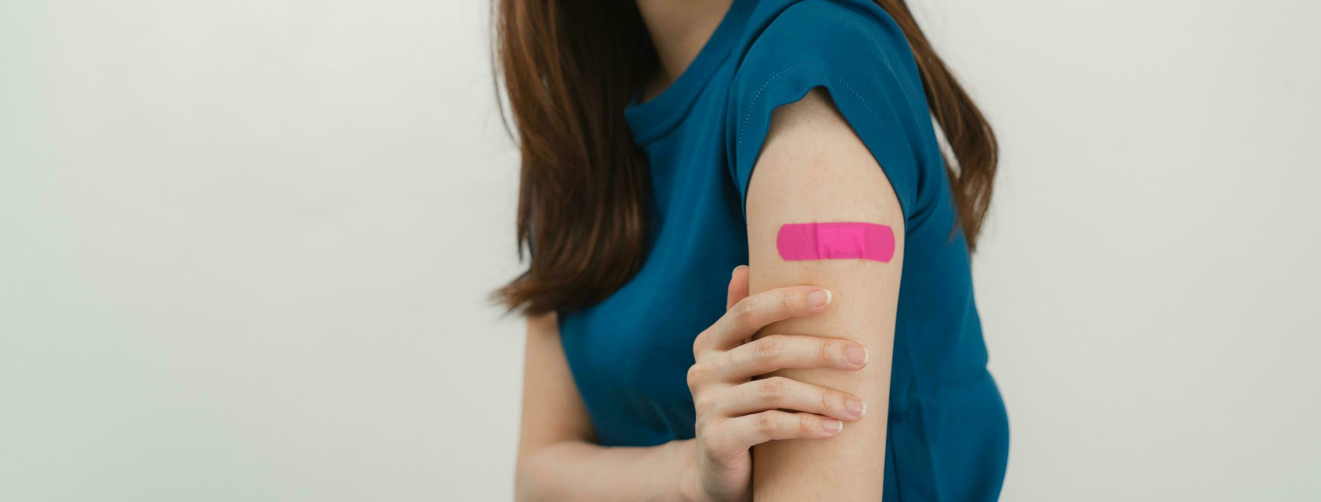 dichtbij omhoog tiener- aantrekkelijk Aziatisch jong, na krijgen, te ontvangen anti virus vaccin covid19. tonen arm Aan roze verband in blauw t-shirt geïsoleerd Aan wit achtergrond, kopiëren ruimte. foto