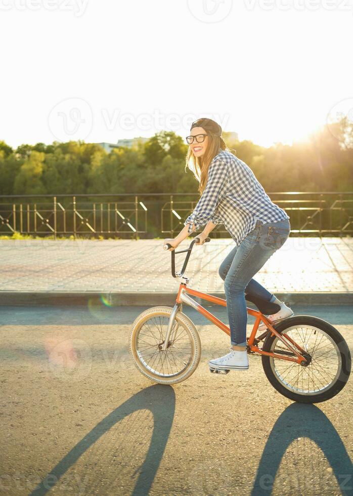 lief jong vrouw in een hoed rijden een fiets Aan stad achtergrond in de zonlicht buitenshuis foto