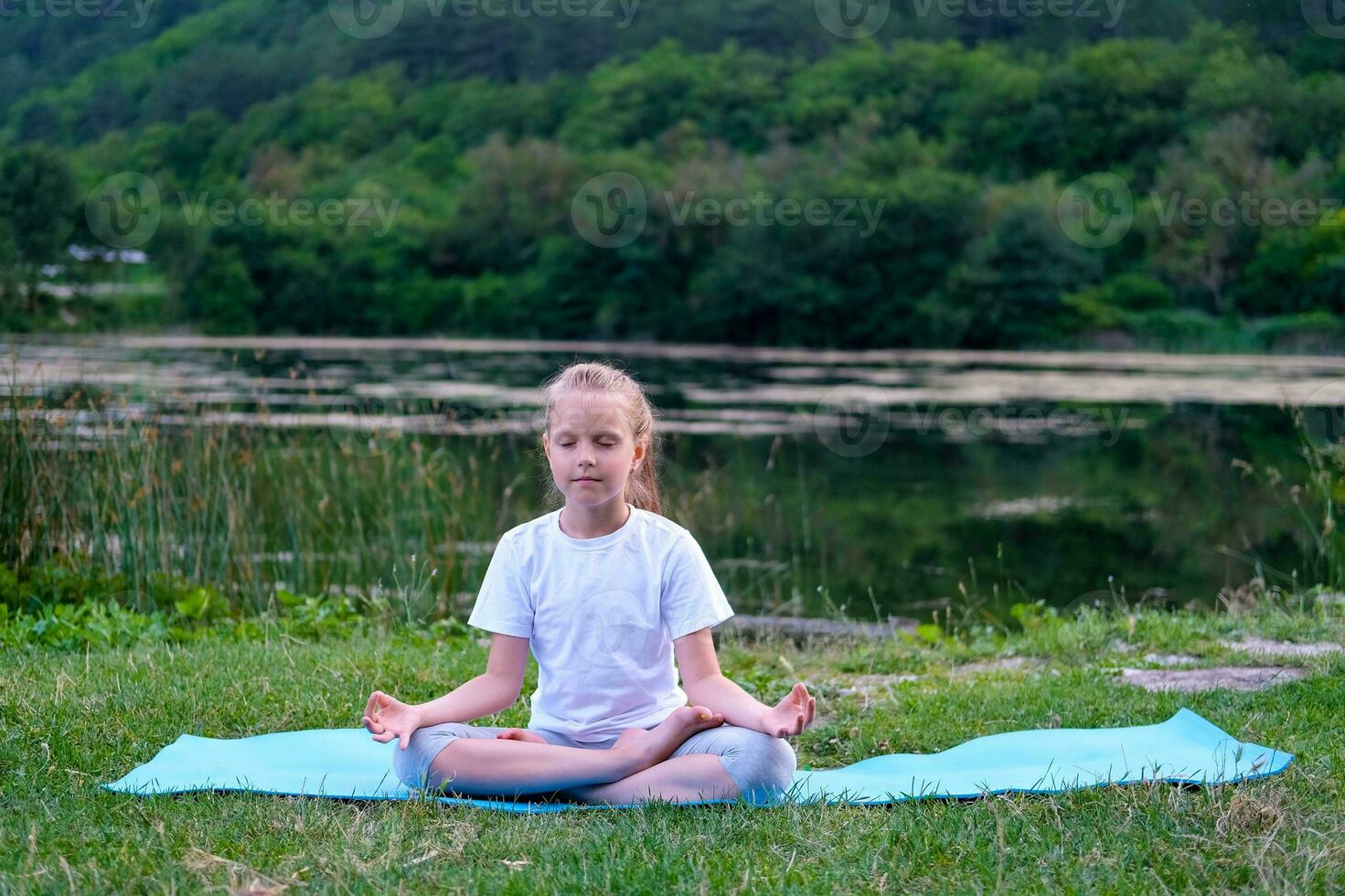 mooi gelukkig meisje met Gesloten ogen beoefenen yoga in de lotus positie in de buurt de meer in natuur. foto