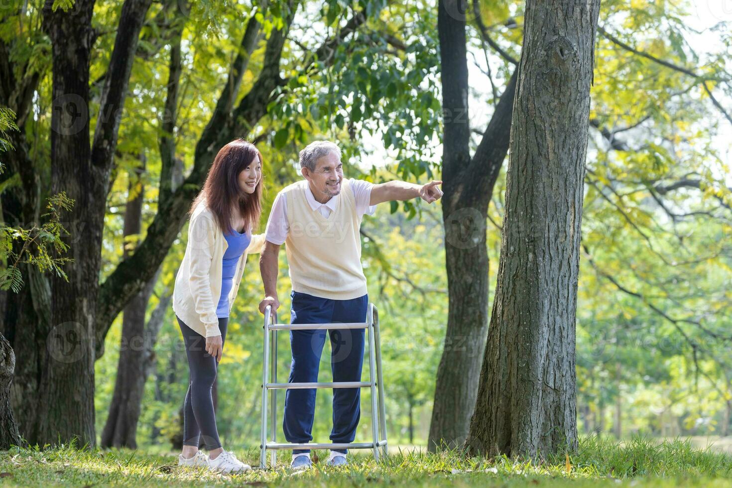 Aziatisch senior Mens met wandelaar en zijn dochter wandelen samen in de park op zoek voor mooi natuur en dieren in het wild gedurende zomer voor licht oefening en fysiek behandeling concept foto