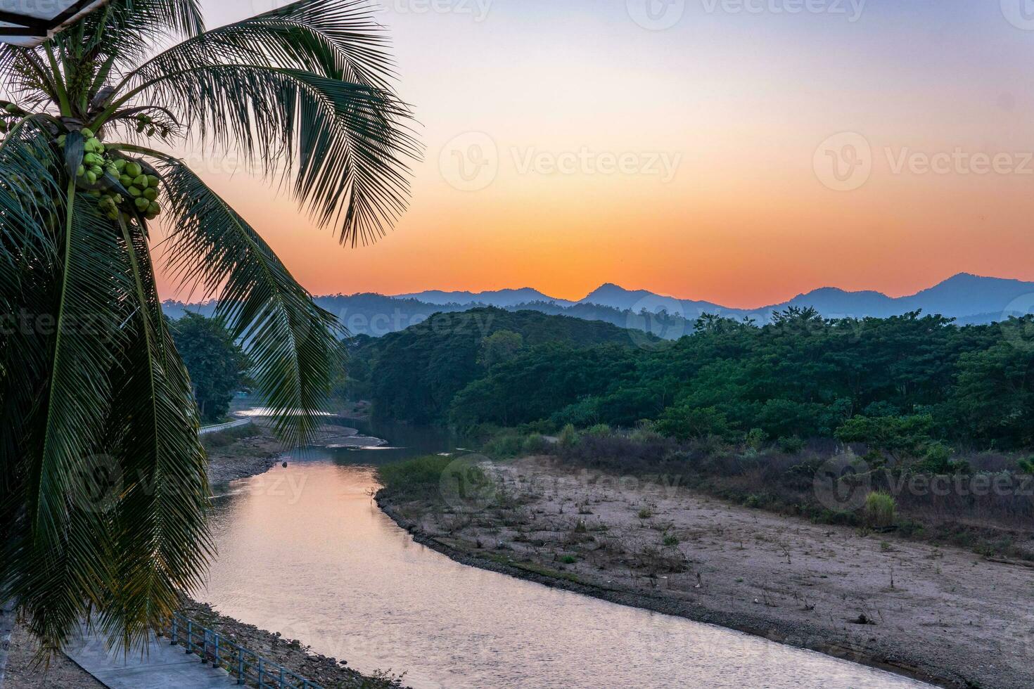 zonsondergang over de bergen met rivier en palmboom foto