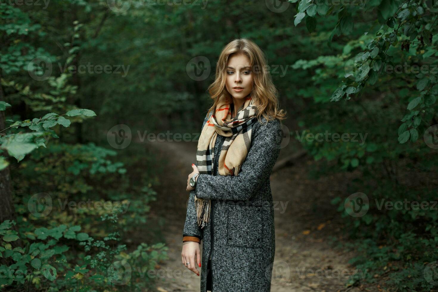 mooi jong vrouw in een gebreid sjaal en herfst jas in de buurt de groen bladeren foto