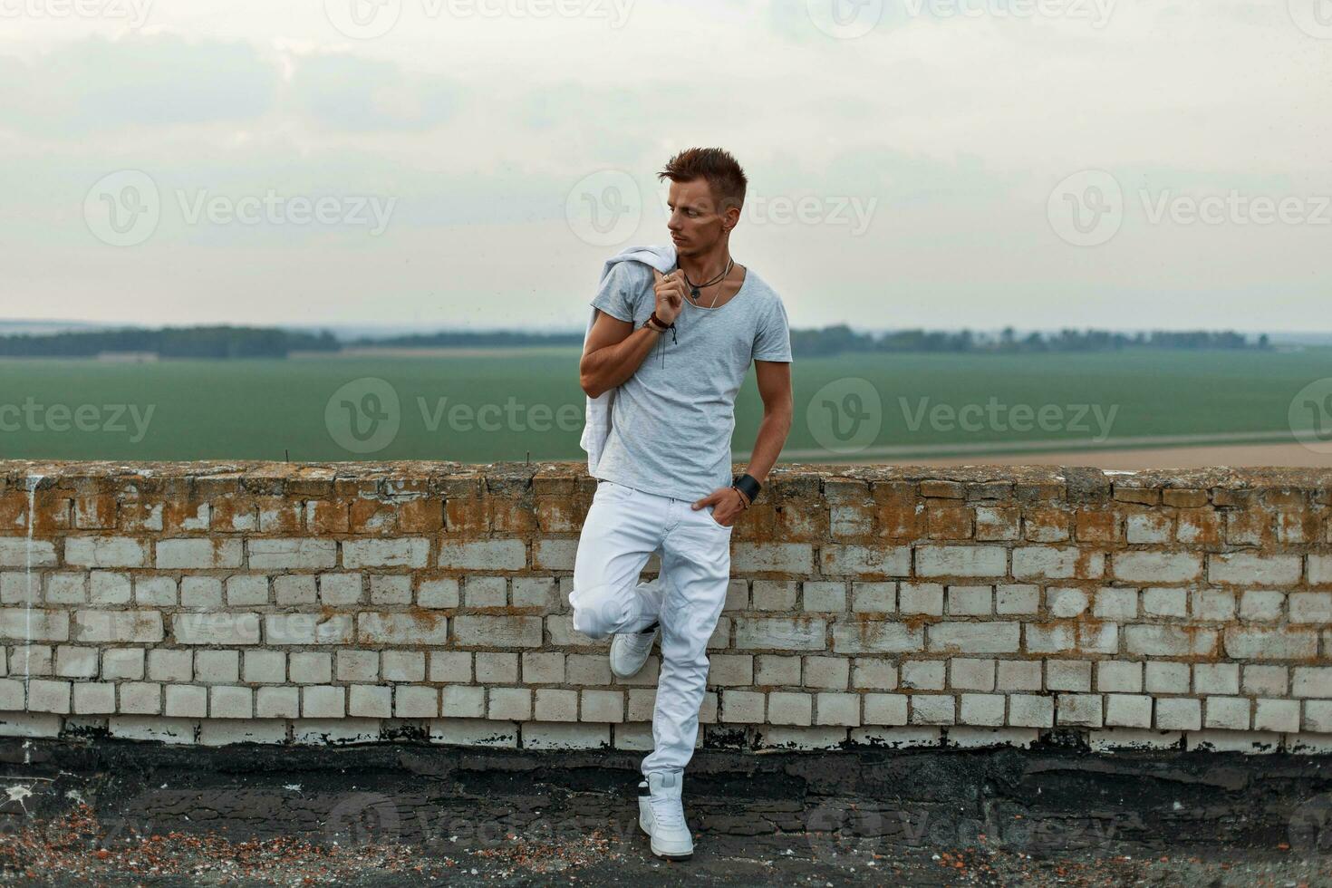 knap Mens in wit kleren staand in de buurt de steen muur Aan de dak. foto