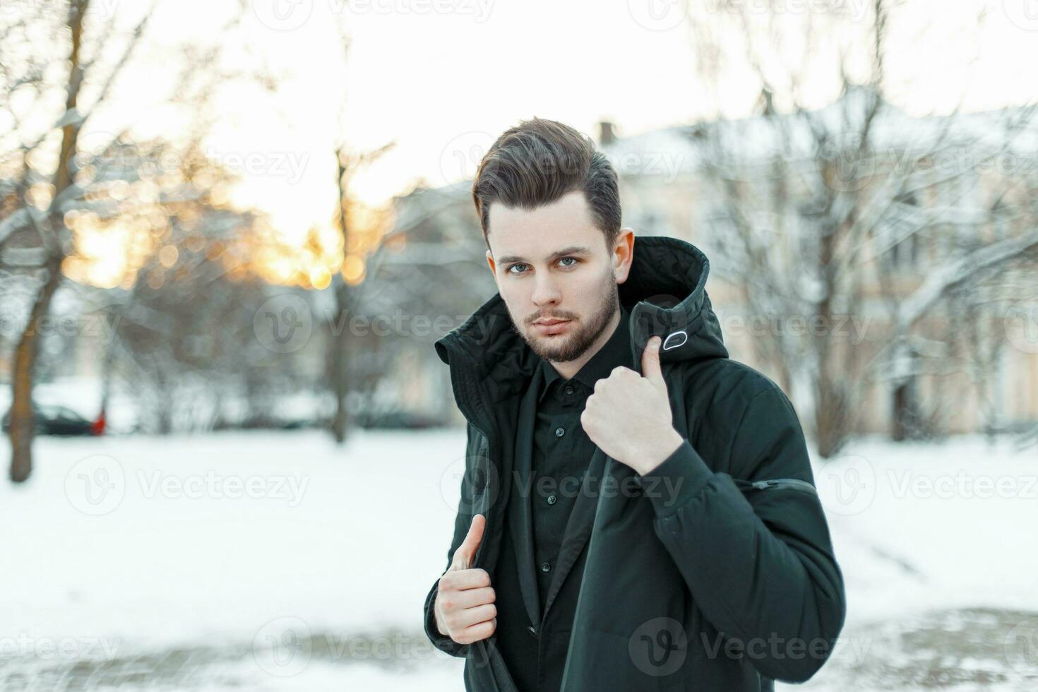 knap jong Mens model- met haar- in een zwart jasje in een besneeuwd park foto