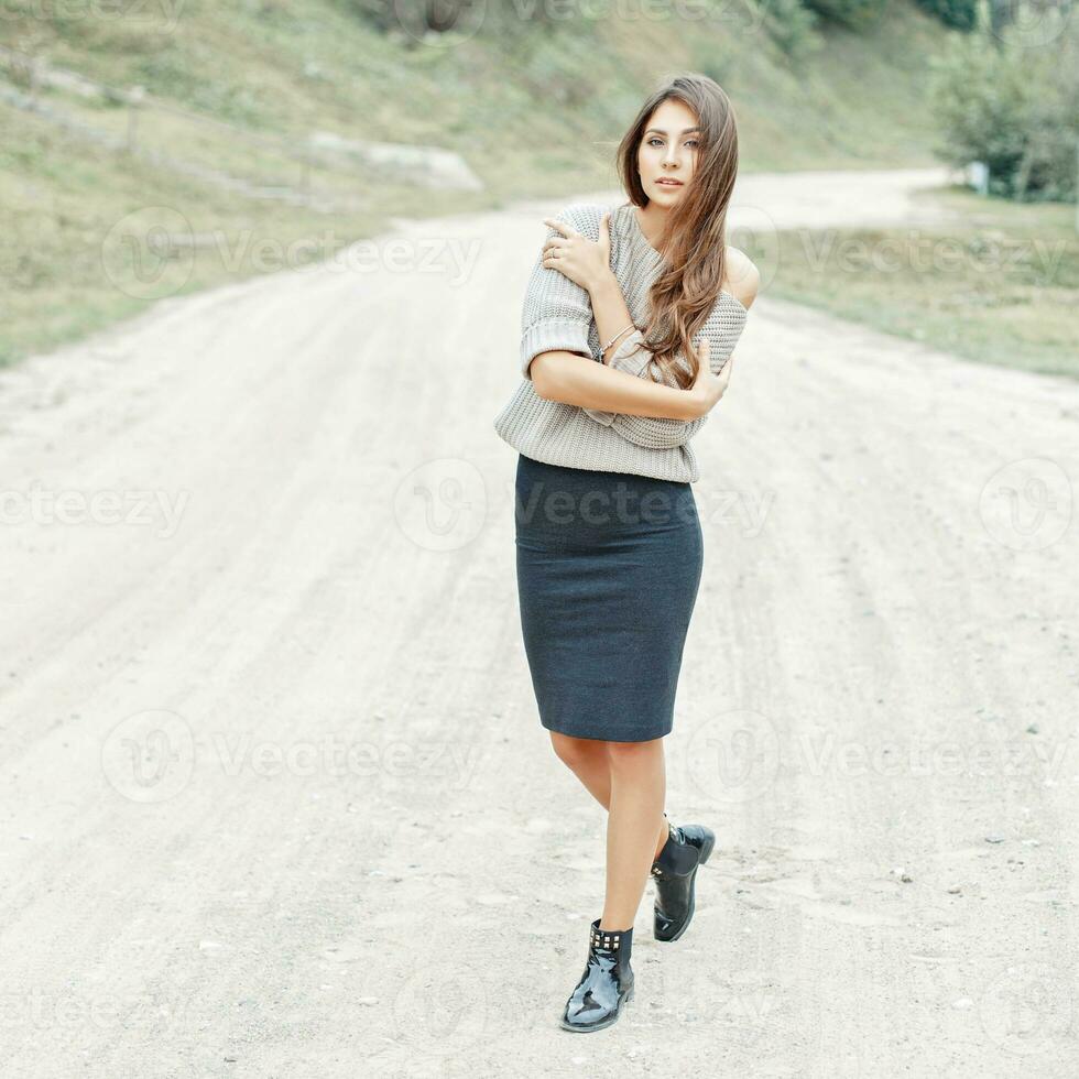 mooi meisje model- in een grijs trui, rok en laarzen wandelen Aan een zand weg. foto