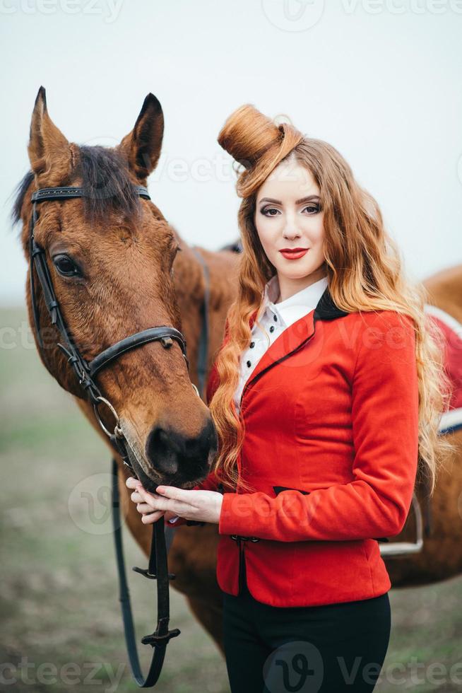 roodharig jockeymeisje in een rood vest en zwarte hoge laarzen met een paard foto