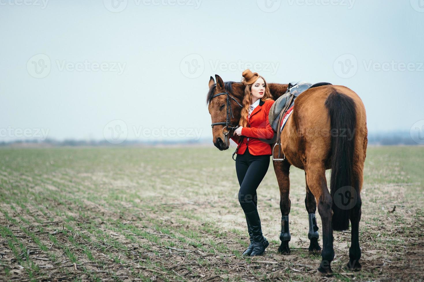 roodharig jockeymeisje in een rood vest en zwarte hoge laarzen met een paard foto