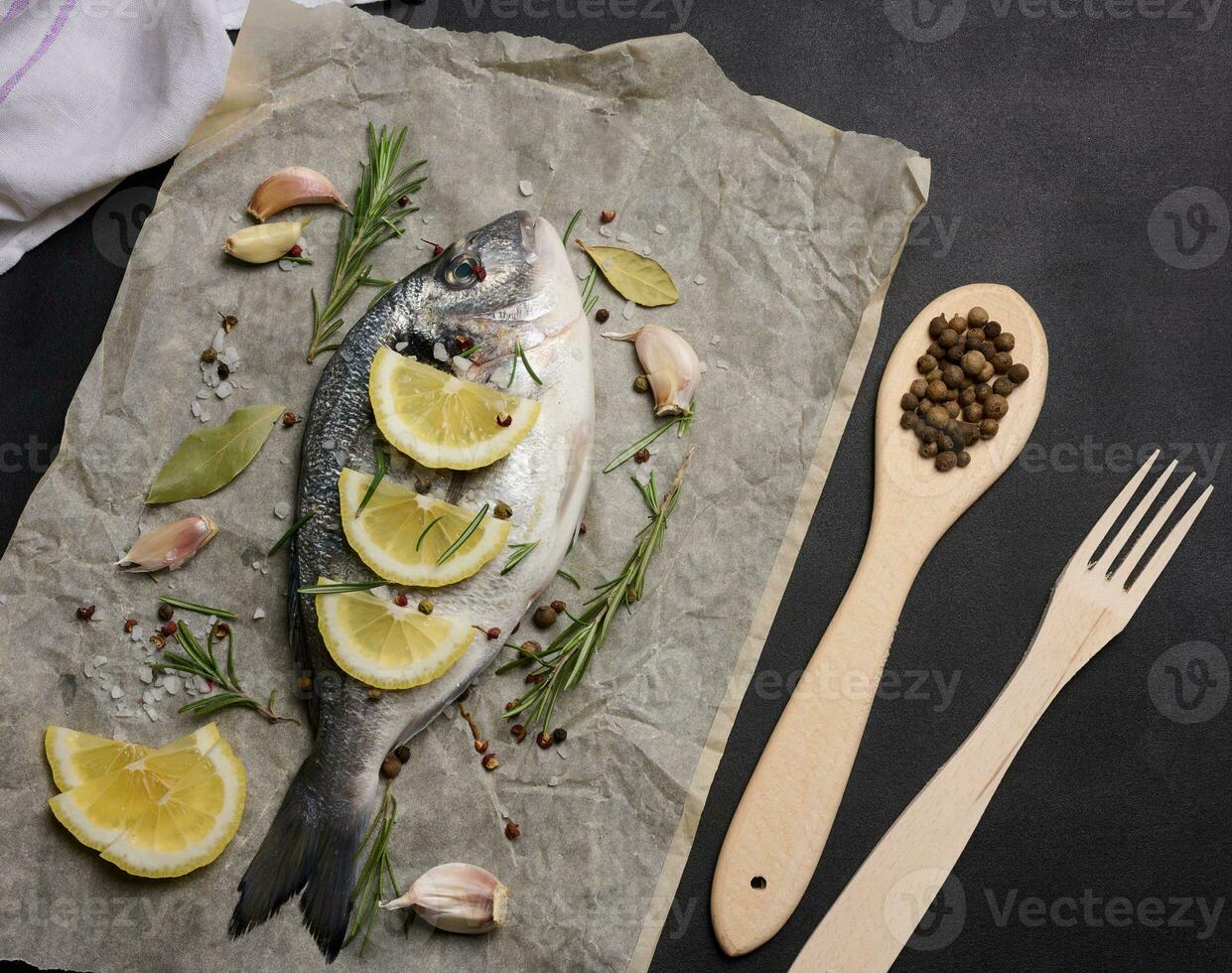 rauw geheel dorado vis Aan bruin perkament papier en specerijen voor Koken, top visie Aan zwart tafel foto