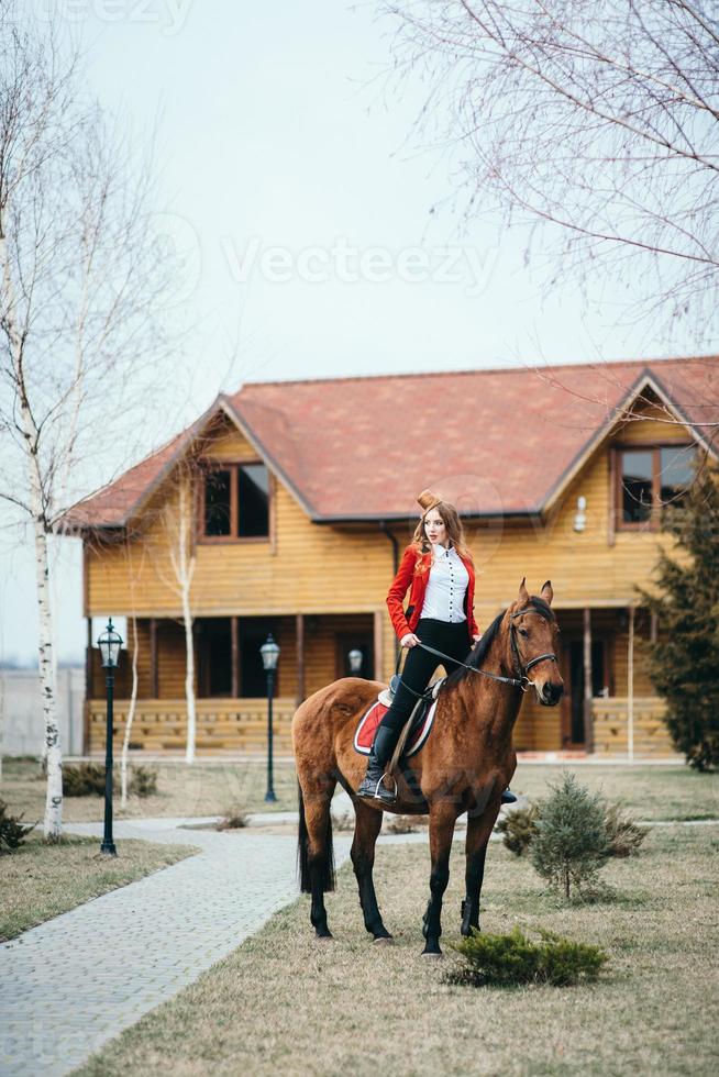 roodharig jockeymeisje in een rood vest en zwarte hoge laarzen met een paard foto