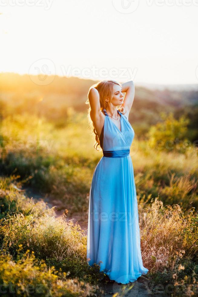 blonde met losse haren in een lichtblauwe jurk in het licht van de zonsondergang foto