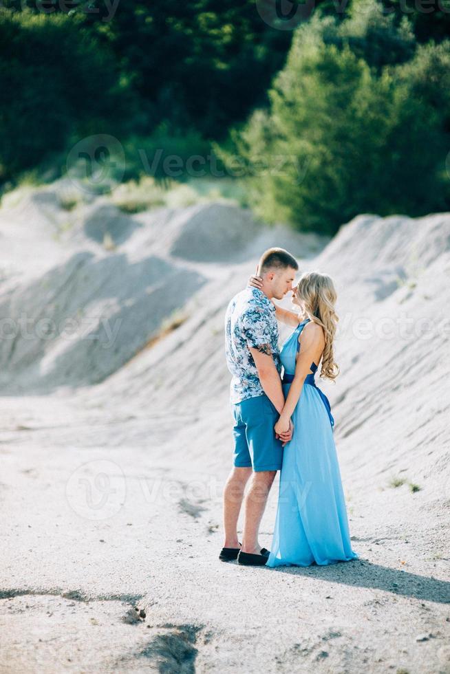 blond meisje in een lichtblauwe jurk en een man in een licht overhemd in een granietgroeve foto