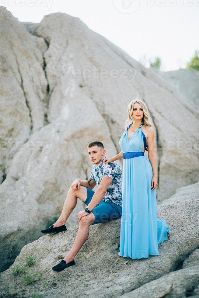 blond meisje in een lichtblauwe jurk en een man in een lichte korte broek in een granietgroeve foto