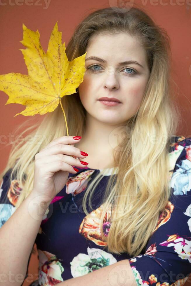 een mooi blond meisje met blauw ogen is Holding een esdoorn- blad. foto