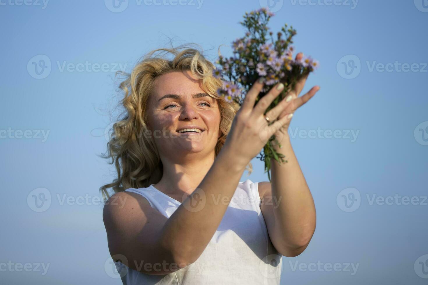 mooi middelbare leeftijd blond met een boeket van wilde bloemen tegen de blauw lucht. foto