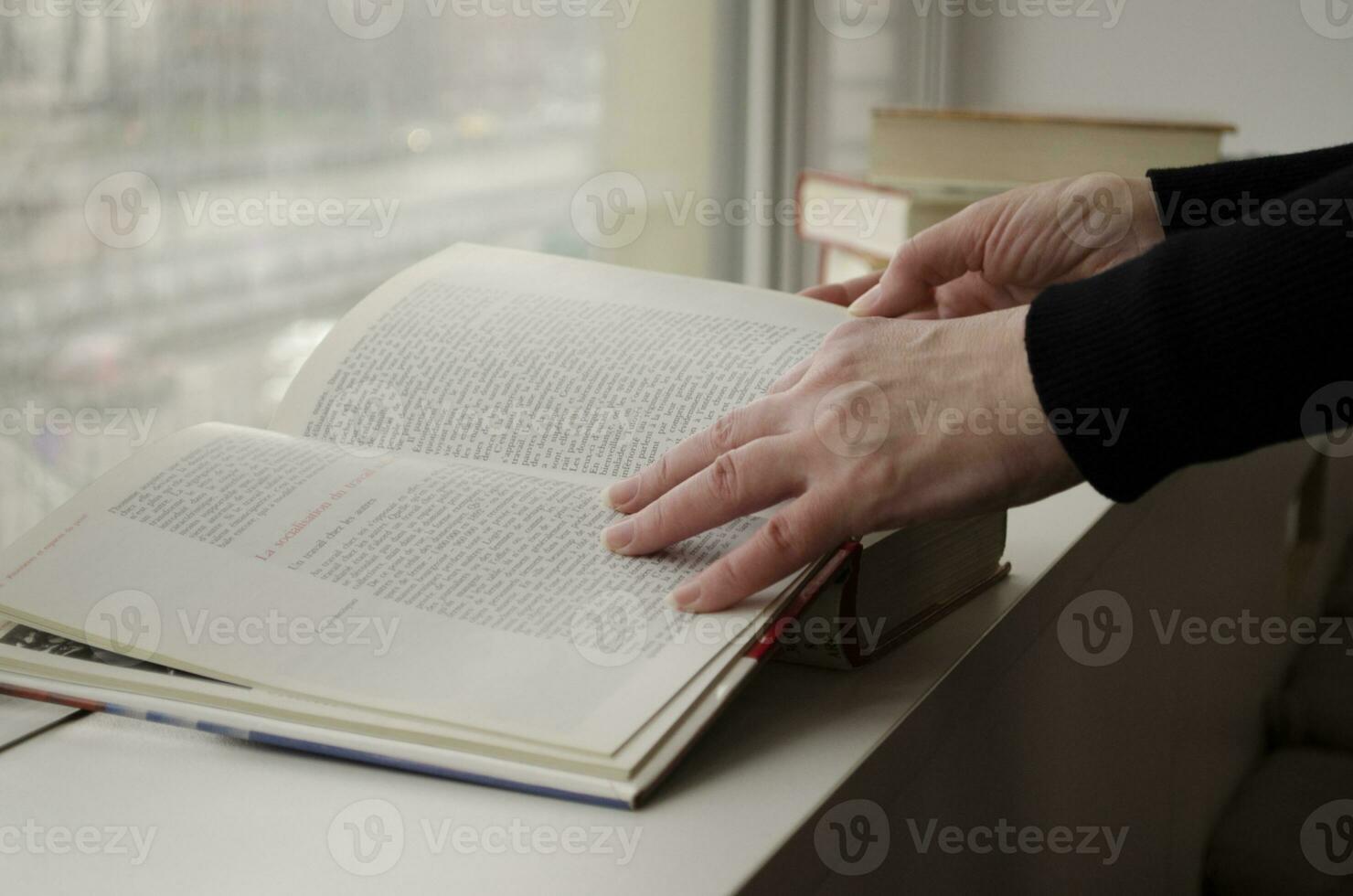 een persoon lezing boeken in de buurt de venster. handen bochten over- boek bladzijde. foto