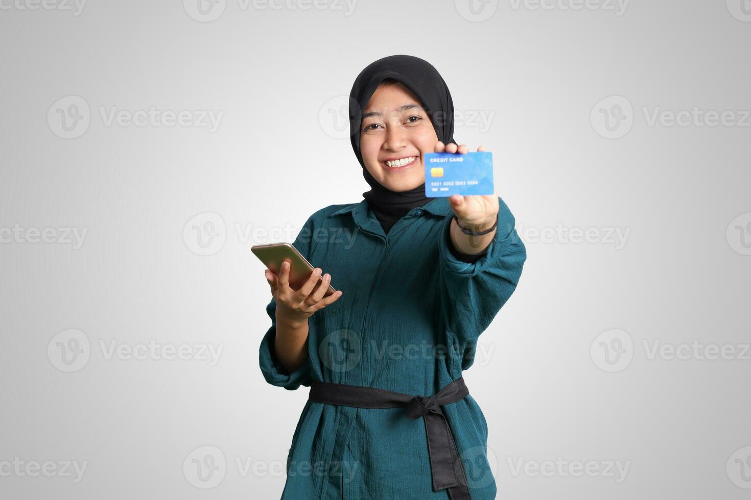 portret van vrolijk Aziatisch moslim vrouw met hijaab, tonen credit kaart terwijl Holding mobiel telefoon. financieel en spaargeld concept. geïsoleerd beeld Aan wit achtergrond foto