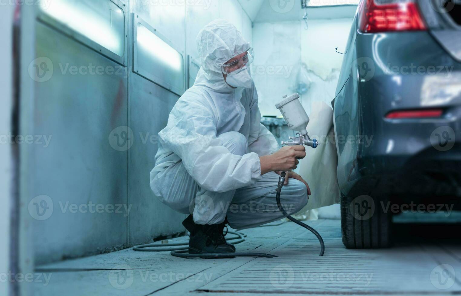 monteur schilderij auto in kamer. arbeider gebruik makend van verstuiven geweer en airbrush en schilderij een auto, garage schilderij auto onderhoud reparatie en onderhoud foto