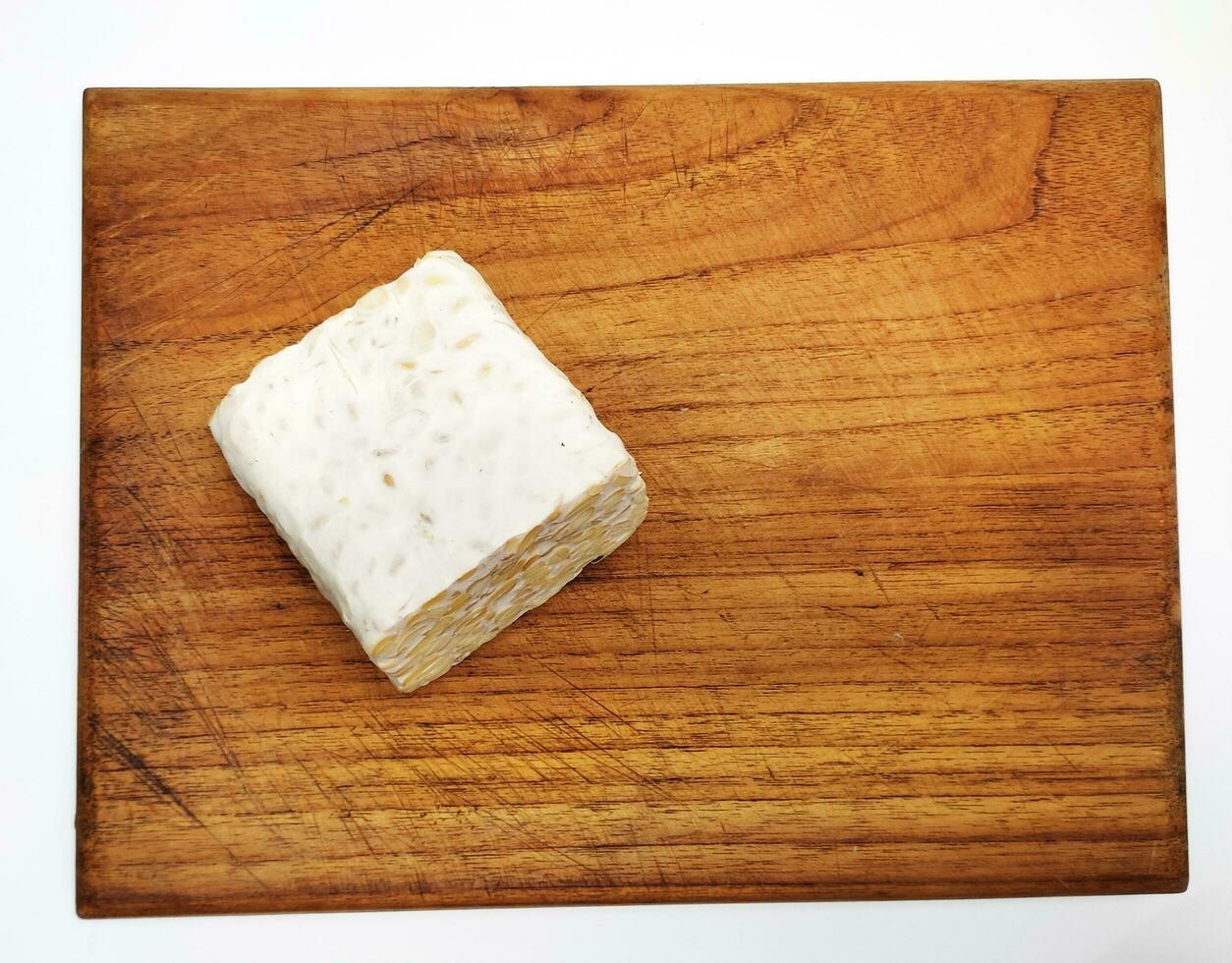 rauw tempeh of tempo, Indonesisch traditioneel voedsel, gemaakt van gefermenteerd soja bonen, Aan houten snijdend bord, Aan wit achtergrond. foto