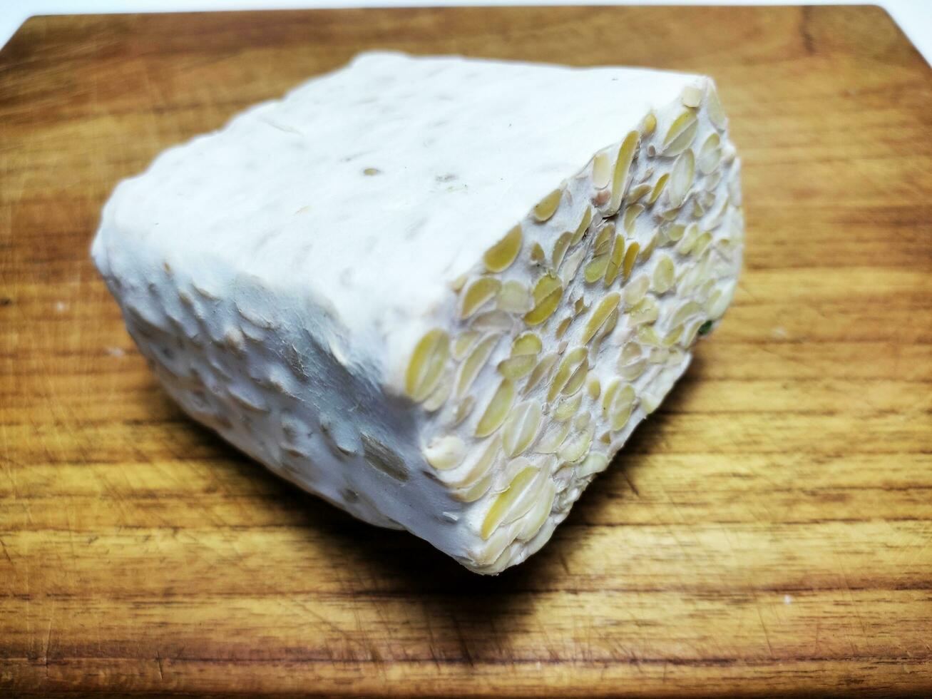 rauw tempeh of tempo, Indonesisch traditioneel voedsel, gemaakt van gefermenteerd soja bonen, Aan houten snijdend bord, Aan wit achtergrond. foto