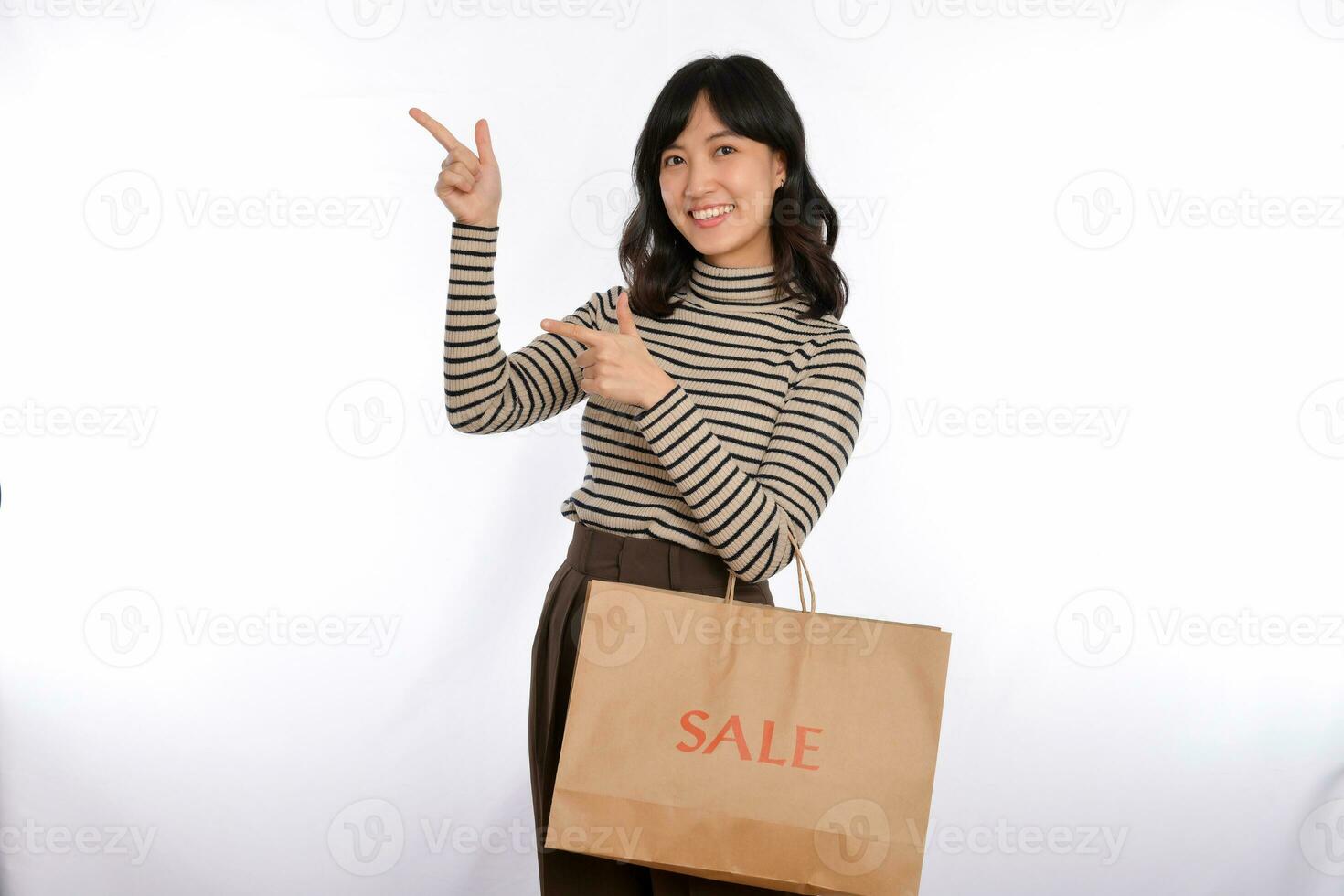 mooi jong Aziatisch vrouw Aan trui kleding richten omhoog naar kopiëren ruimte en op zoek Bij camera met glimlach gezicht en uitverkoop boodschappen doen papier zak geïsoleerd Aan wit achtergrond foto