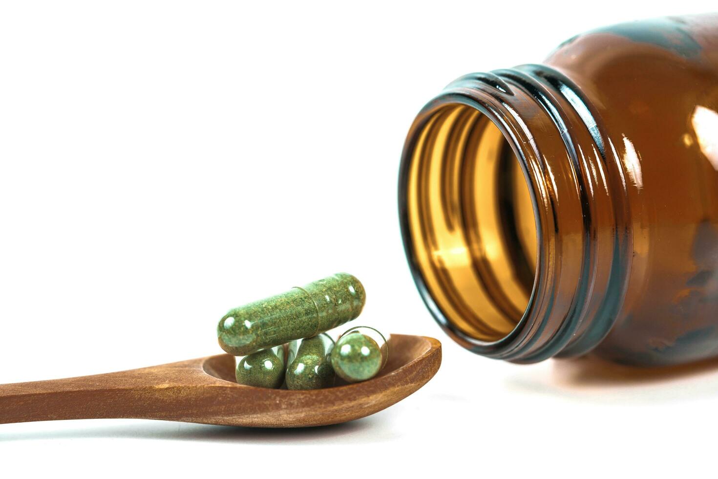 kruiden geneeskunde capsules in hout lepel Aan wit achtergrond foto