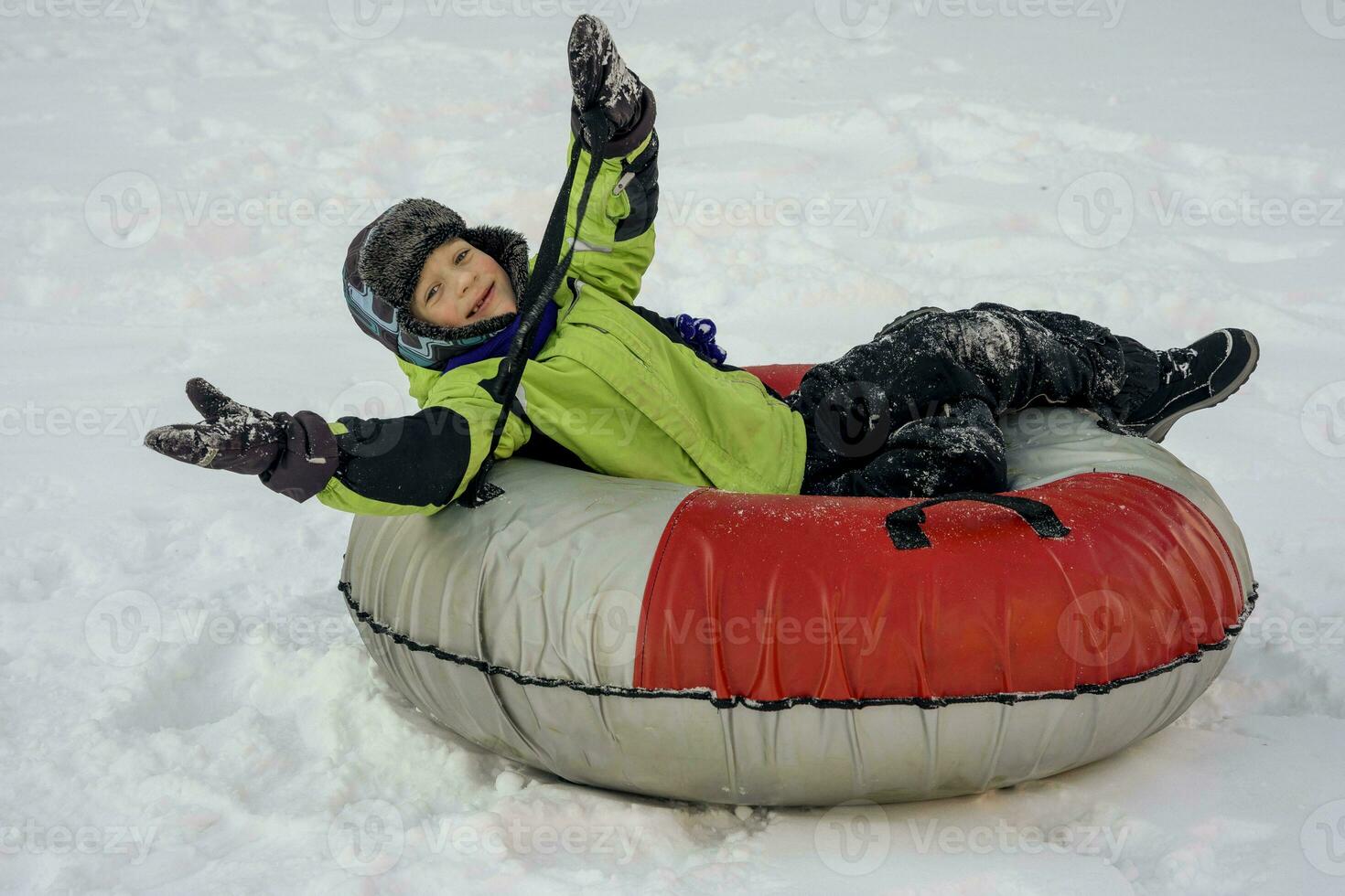 grappig Kaukasisch jongen 5 jaren oud ritten in winter Aan een groot opblaasbaar kwarktaart foto