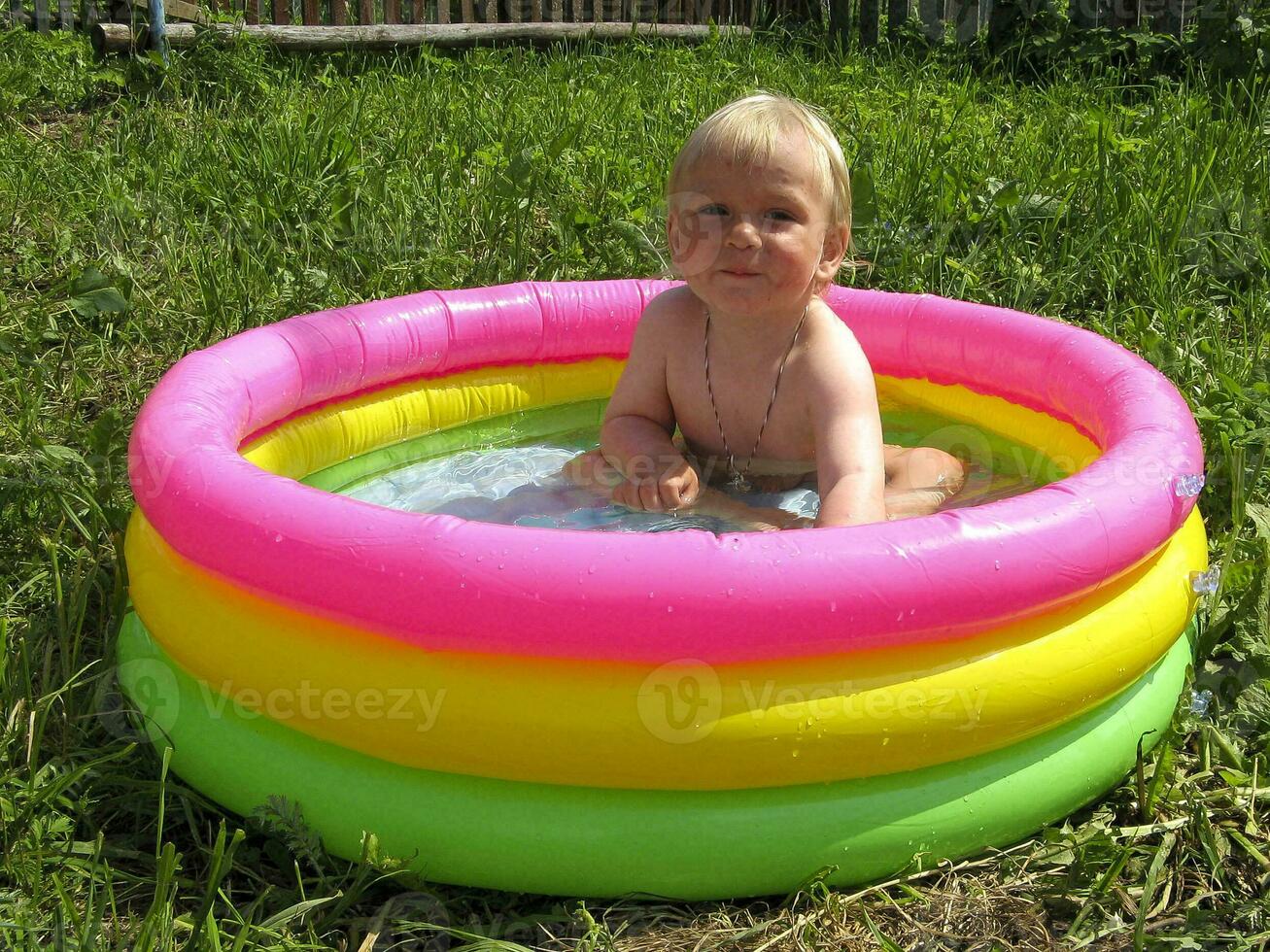 kind is zittend in een kleurrijk opblaasbaar zwembad met water in zomer foto